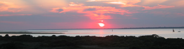Multicolored September sunset over Bellport Bay with silhouette of small watercraft and sailboat.