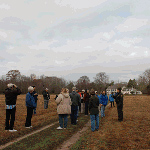 Ranger with group in field in front of historic house during fall tour.