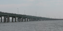 The uppermost level of a long bridge sloping down to the island is covered by a string of cars and vans. The uppermost level of a long bridge sloping down to the island is covered by a string of cars and vans.