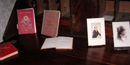 Three hard-bound books and portraits from the late 1800s are lined up on a dark table. Three hard-bound books and portraits from the late 1800s are lined up on a dark table.