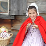 a little girl ties a bright red cape aroud her shoulders. she smiles warmly