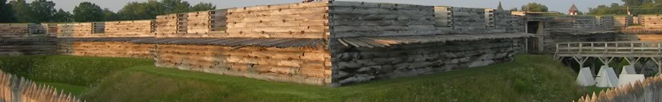 large wooden spikes jut out from a large wooden angular wall lit by sunlight. verdant grass surrounds it.