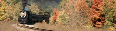 Steam locomotive pulling passenger train through fall colors in the Pocono Mountains.