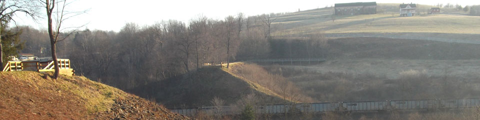 A view of the South and North abutments of the South Fork Dam.  The Visitor Center, Unger House, and Spring House are visible in the background.  As is visible, a spur railroad line connects coal trains with the main line of the railroad.