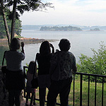 Four people standing on the shore looking at an island through binoculars