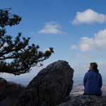 Hiker seated on rock with blue sky.