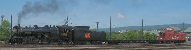 Steam engine Canadian National 3254, a freight locomotivebuilt in 1917, pulls a flat car and caboose in the railroad yard at Steamtown.