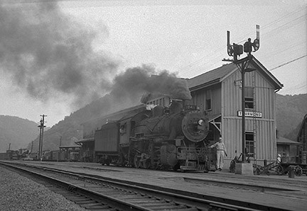 Old picture of a large steam locomotive and engineer in front of a wooden train depot with a sign that says Thurmond