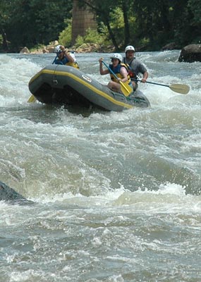 Three individuals ride through a white water rapid on the New River in West Virginia.