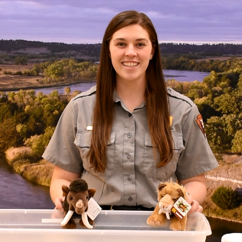 A Ranger holds two stuffed animals while presenting.
