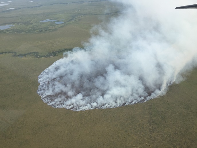 Aerial view of tundra with a round swatch burning and smoking.