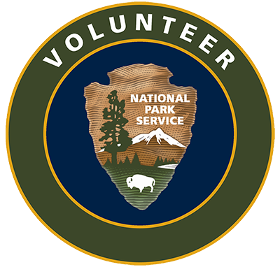 National Park Service Arrowhead on a field of blue with a green circle around it. Text in the green circle reads "Volunteer."