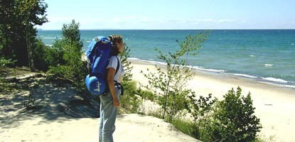Backpacker standing on a viewpoint overlooking a sandy shore and large lake on a sunny day.