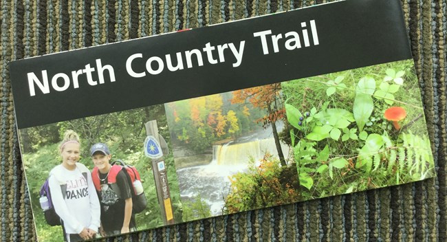 Front cover of the North Country Trail brochure shows the trail name in a black title band with three photos below. The three photos show to young hikers, a waterfall, and small forest floor plants.