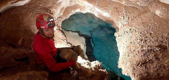 Man sitting above blue lake within cave