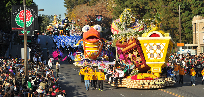 Crowds stand watching colorful floats and marchers pass by at the Rose Parade