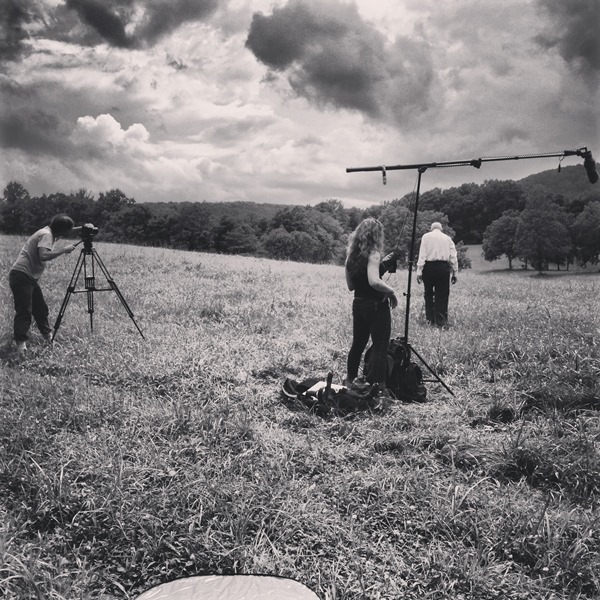 filming crew standing in field with old man doing interview