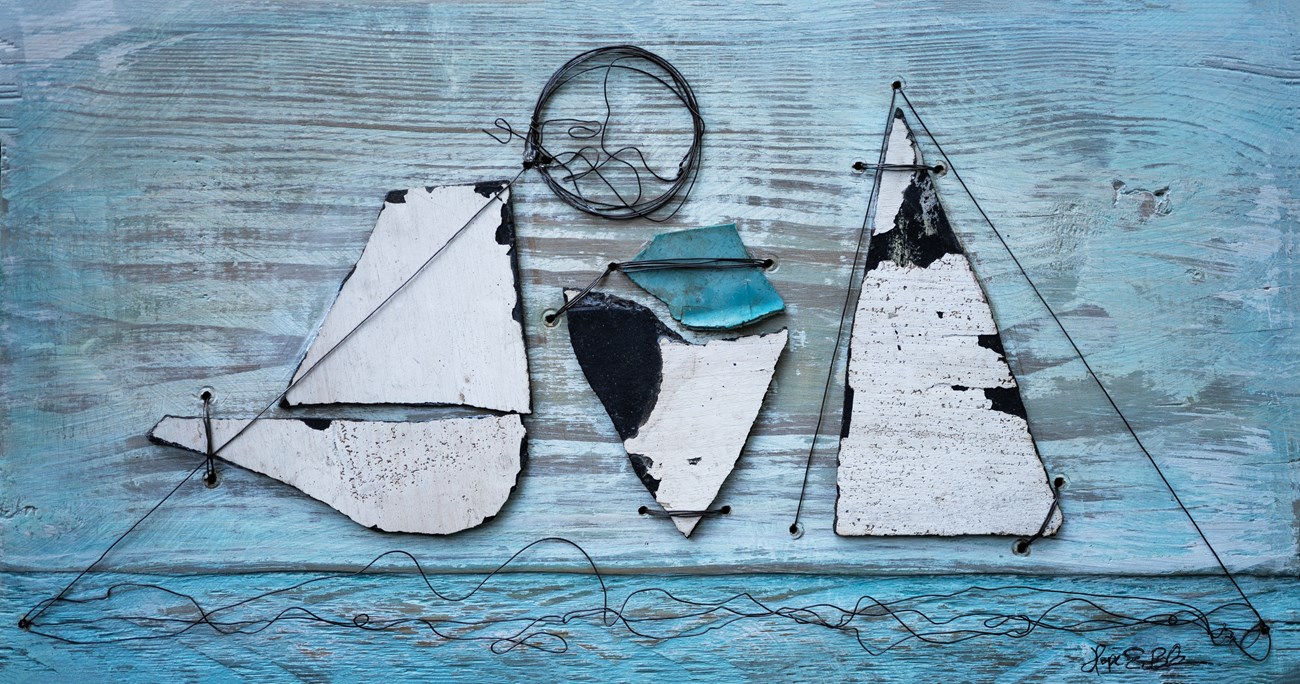 Objects arranged on a background of wood, painted in fading blue. These bits of wire, metal, and paint-chipped slabs form the shape of a snow-capped mountain with a blue shape in the center.
