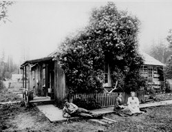 Historic photo of two women and a man outside of a homestead on Lake Ozette