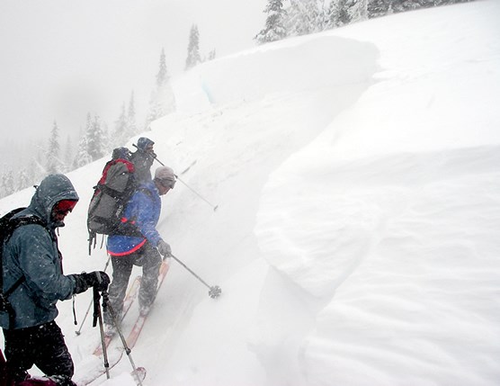 three people standing on snow-covered slope, studying recent avalanche