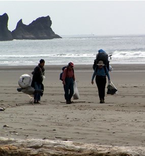 three people carrying large bundles on sandy beach