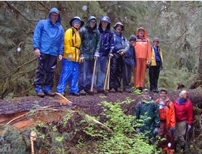 eleven people, all dressed in raingear, standing on and beside large fallen tree
