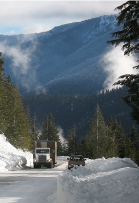 large trailer being pulled up snow-covered road by truck