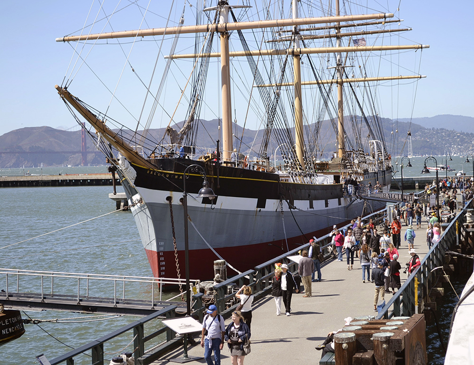 Crowd visiting a historic frigate docked at a pier