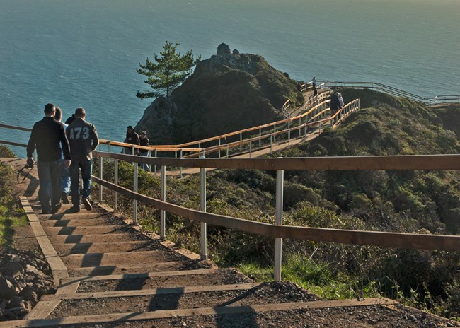 People walk up and down a series of steps as the sun rises on the Muir Beach Overlook, a trail with wide ocean views.