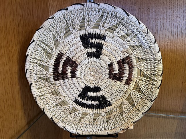 A beautiful pale yellow grass basket with several black "S" shaped designs weaved through it.