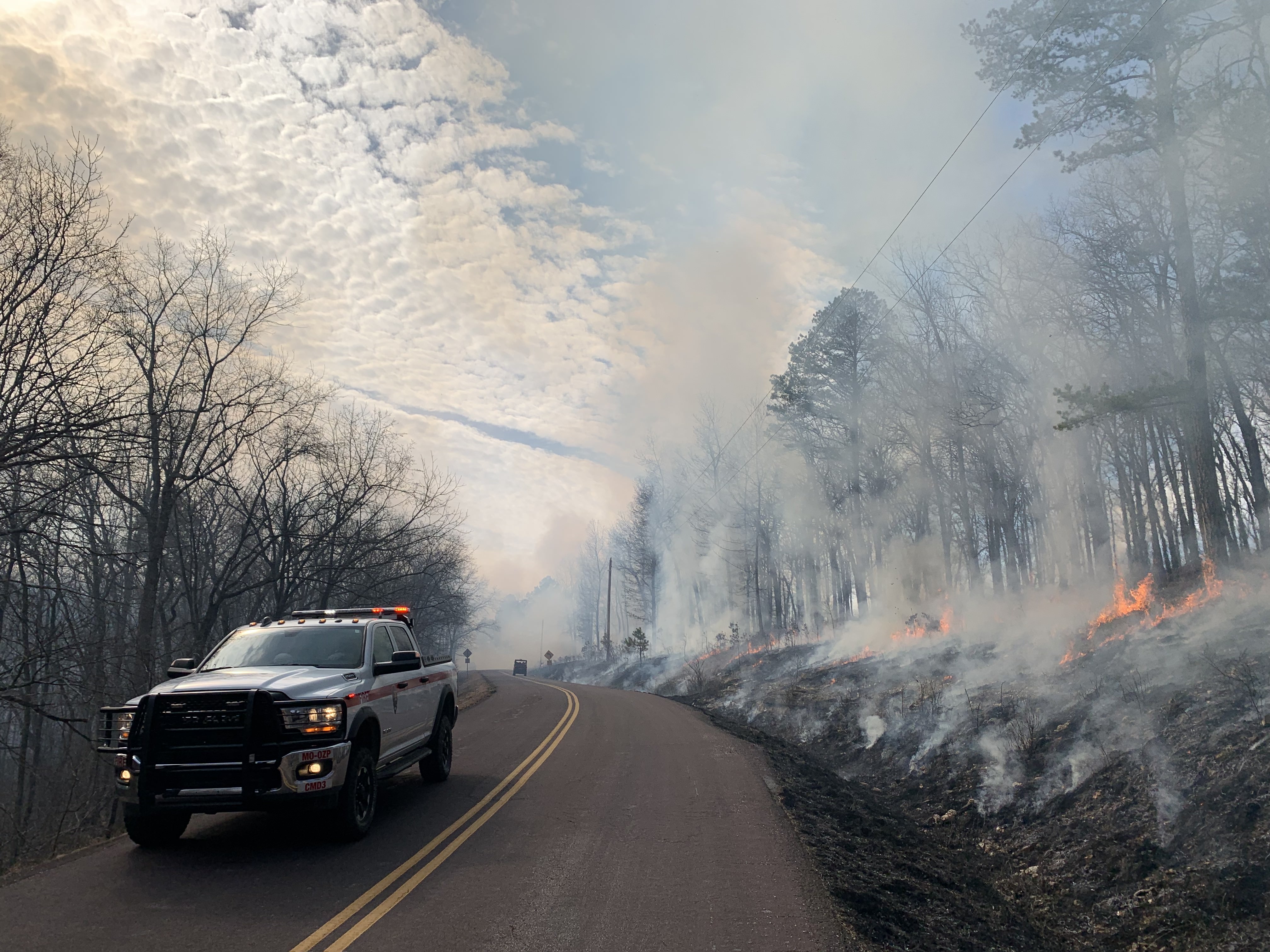 A national park service fire truck in country 2-lane highway with a smokey forest scene just off the road.