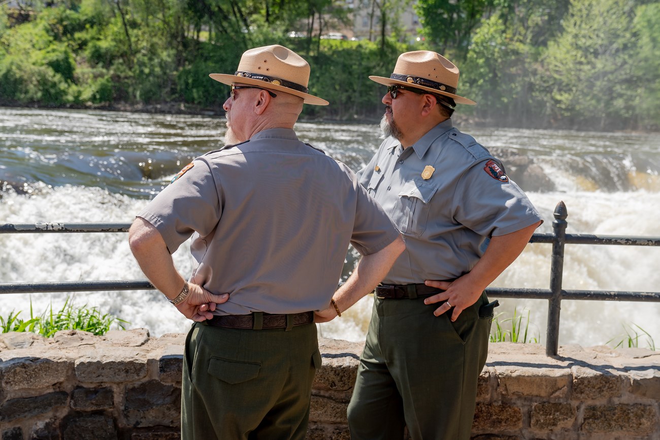 Park Superintendent Darren Boch & director of the National Park Service Charles F. Sams III stand in uniform observing the falls of the Passaic from an overlook