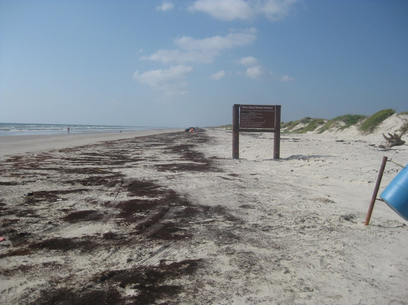 A sandy beach with a brown sign in the center.