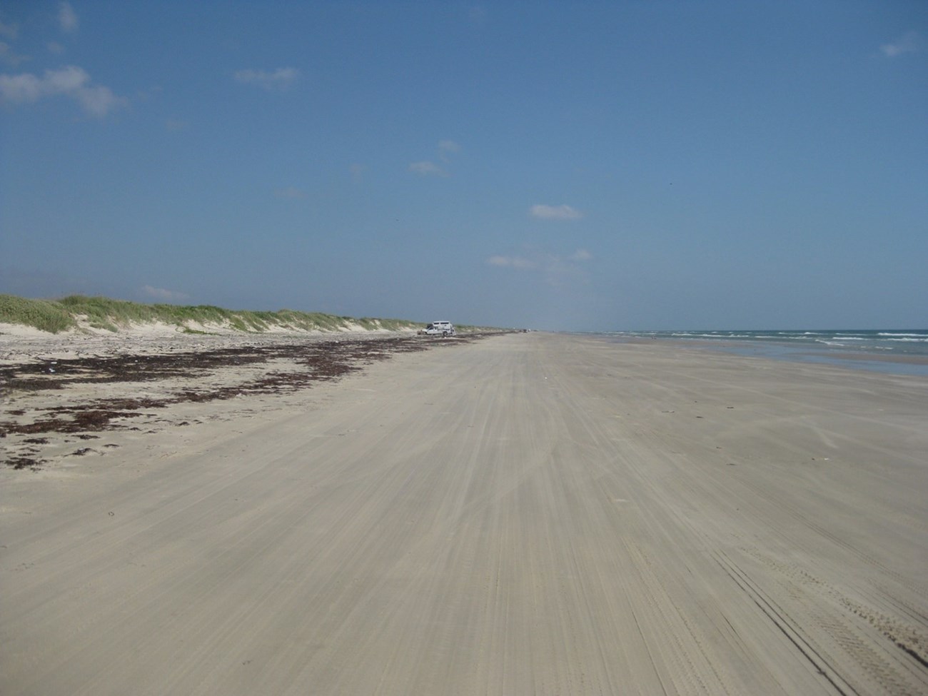 A long sandy beach with dunes on the left side and water on the right.