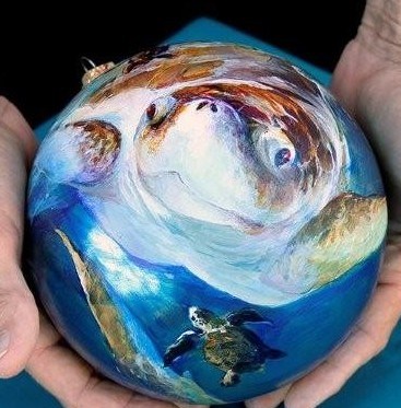 Two hands holding a round Christmas tree ornament with sea turtles painted on it.