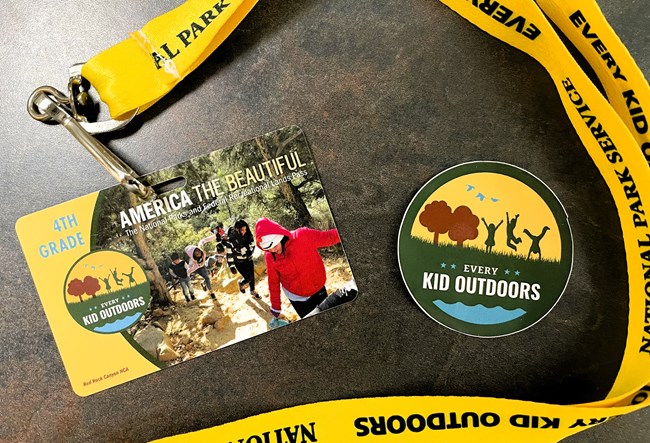 An Every Kid Outdoors plastic pass card on a yellow lanyard.