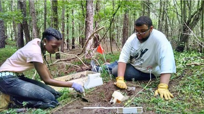 Two youth doing archeology in the woods of Virginia.