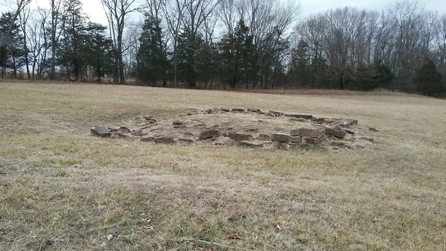 Photo of an old rock foundation, in a grassy field.