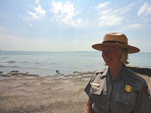 Park Ranger in uniform standing on a beach with Lake Erie in the background.
