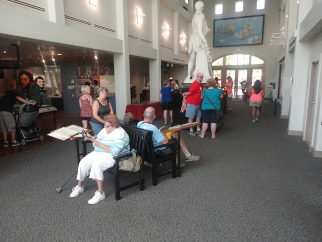 an open entry hall where visitors are sitting near and milling around exhibits including a white marble statue.