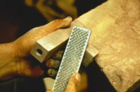 A cultural demonstrator is using a rasp to shape a pipestone bowl