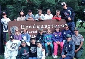 Youth group poses for their photo at the Park Headquarters entrance sign at Sand Point.
