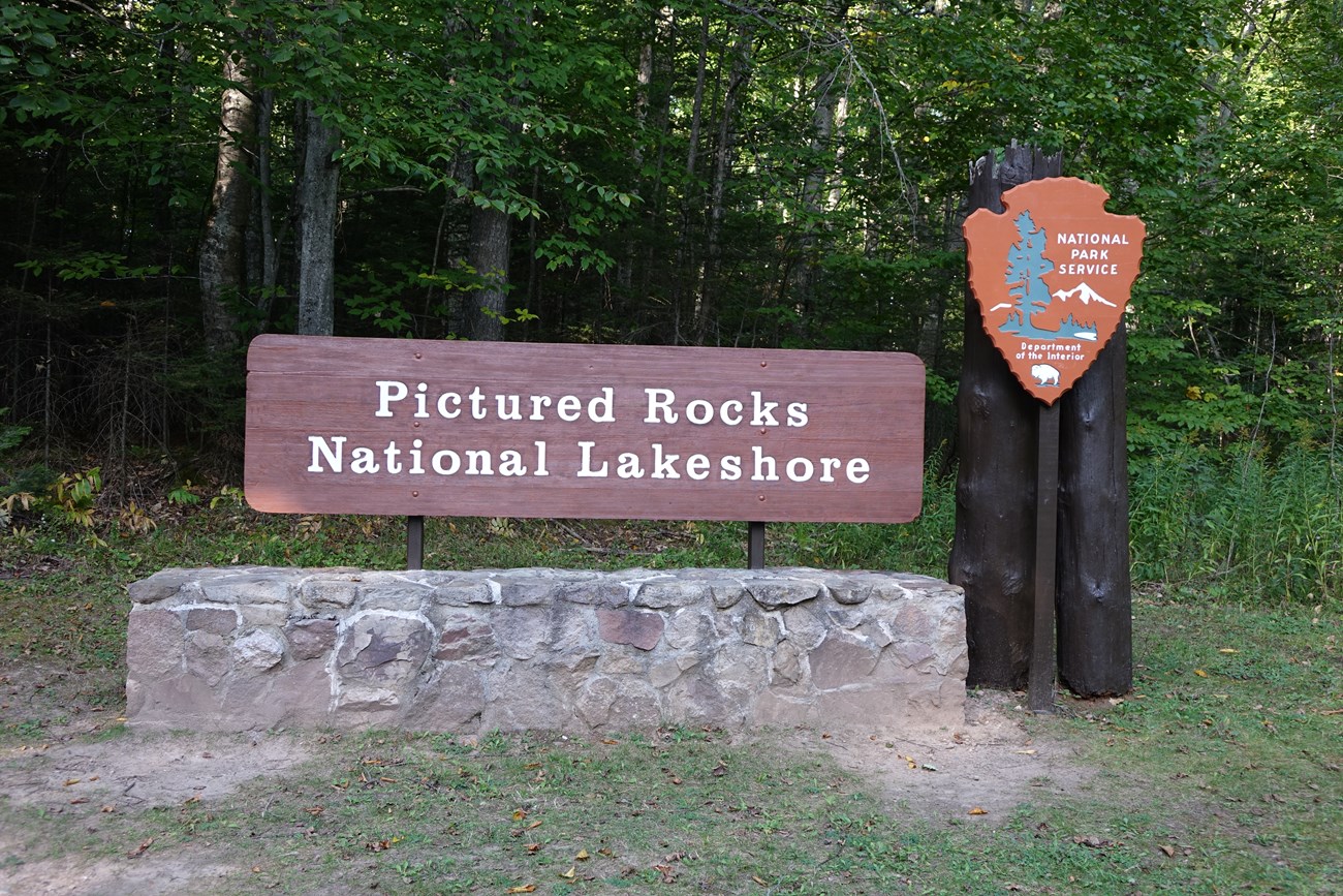 Pictured Rocks National Lakeshore wood park sign on rock base adjacent to wood posts with NPS arrowhead