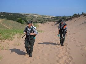 Two members of the invasive plant team hike in the dunes with herbicide in backpack sprayers.