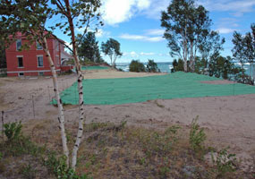 Green stabilization mat covers the ground in front of the red brick head keepers quarters at the Au Sable Light Station. The mat will hold the sand in its place and allow plants to grow.