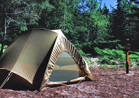 Earth tone brown small tent set up within 15 feet of a numbered post, minimizing visual and ground impact at a backcountry campsite.