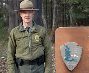 Larry Hach, Chief Ranger at Pictured Rocks National Lakeshore, stands next to the NPS arrowhead.