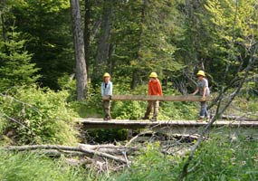 Three Youth Conservation Corps enrollees carry a timber over the Sable Creek bridge.
