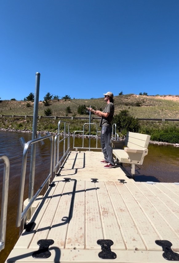 Person fishing from dock that has railings and a bench