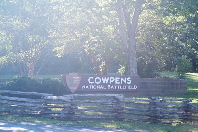 Sunlight washes the park sign and split rail fence at the front gate.